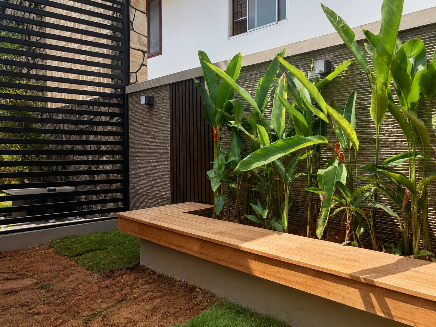 Exterior teak bench beside a tropical planting bed